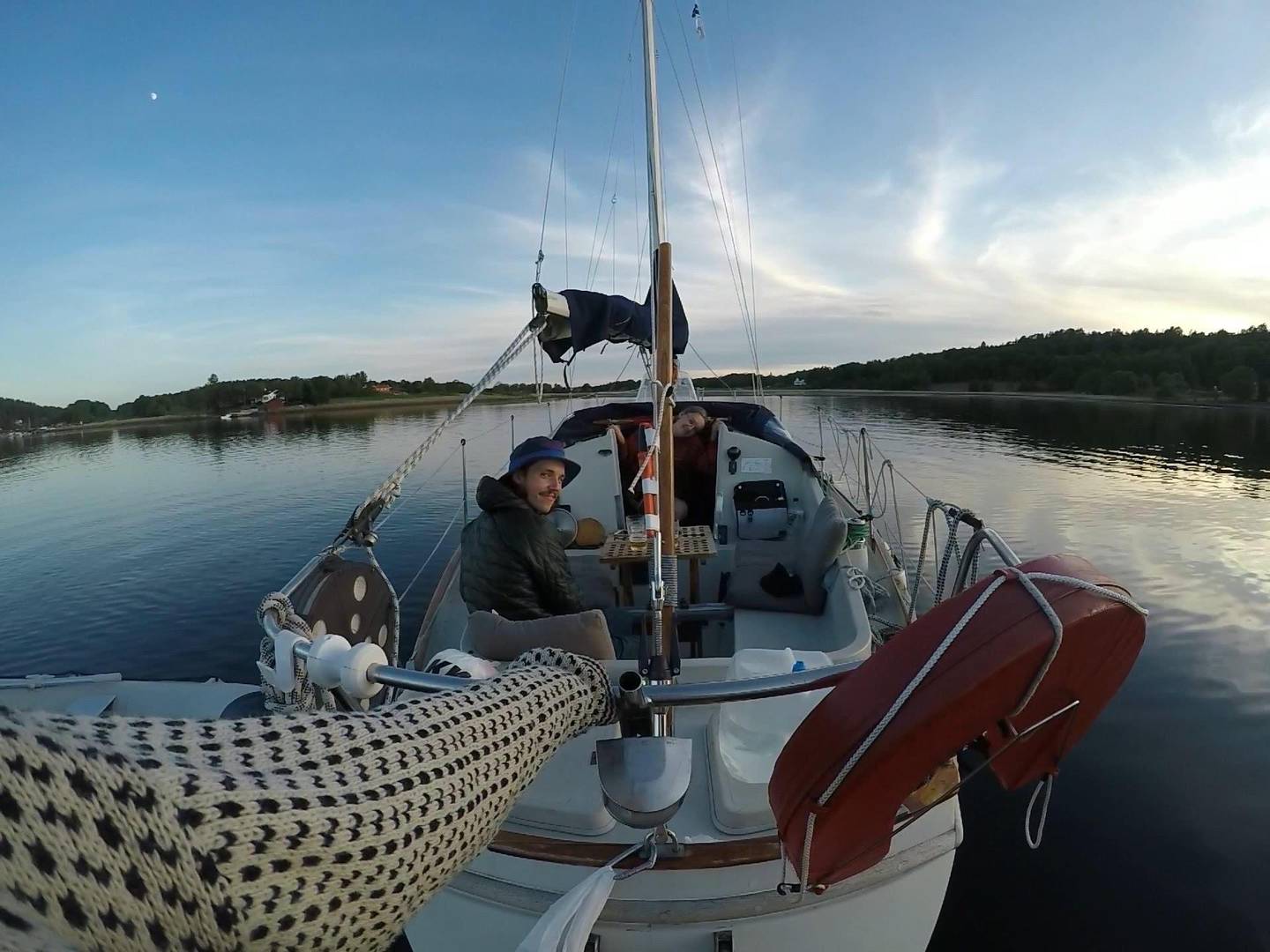 Bildet er av en seilbåt. Det er også mulig å se armen til fotografen som holder seg fast bak båten for å ta et bilde av hele båten ute på vannet.