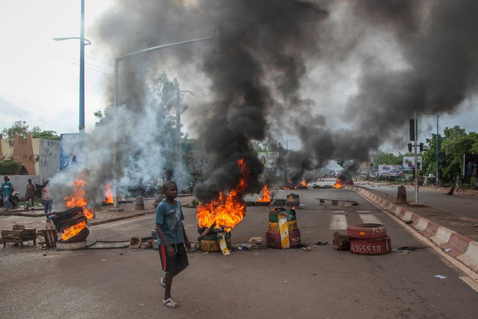 Bildet er fra en demonstrasjon i Malis hovedstad. En gutt går foran brennende sperringer som ligger midt i en bilvei. Det er mye røyk, og lite folk i bildet.