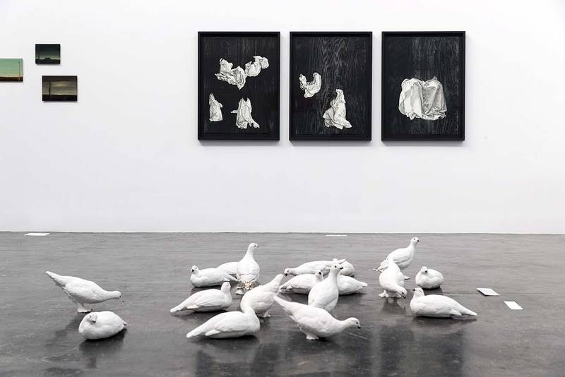 Bildet viser en skulptur av hvite duer laget av Marit Ellisiv Landsend. På veggen bak henger et tresnitt av Nina Björkendal. Det viser noe som ser ut som hvite laken eller kapper.