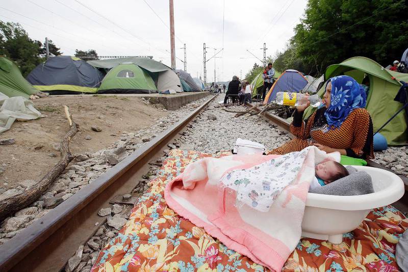 Bildet viser en ung kvinne som sitter på et jernbanespor og drikker vann. Ved siden av henne sover en baby i en balje.