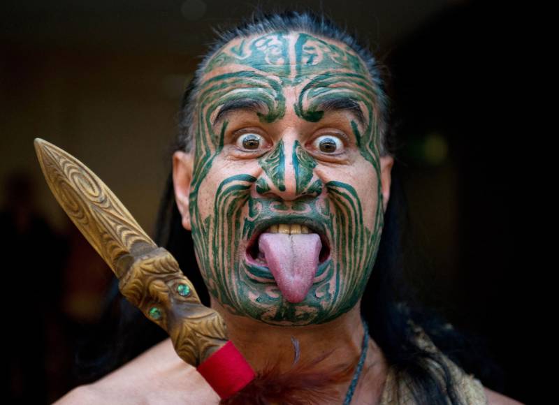 Bildet viser en person fra maori-folket. Han har maling i ansiktet og tunga ute.