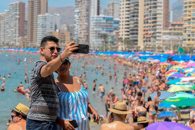 Bildet viser et par som tar selfie på stranda i Benidorm i Spania.