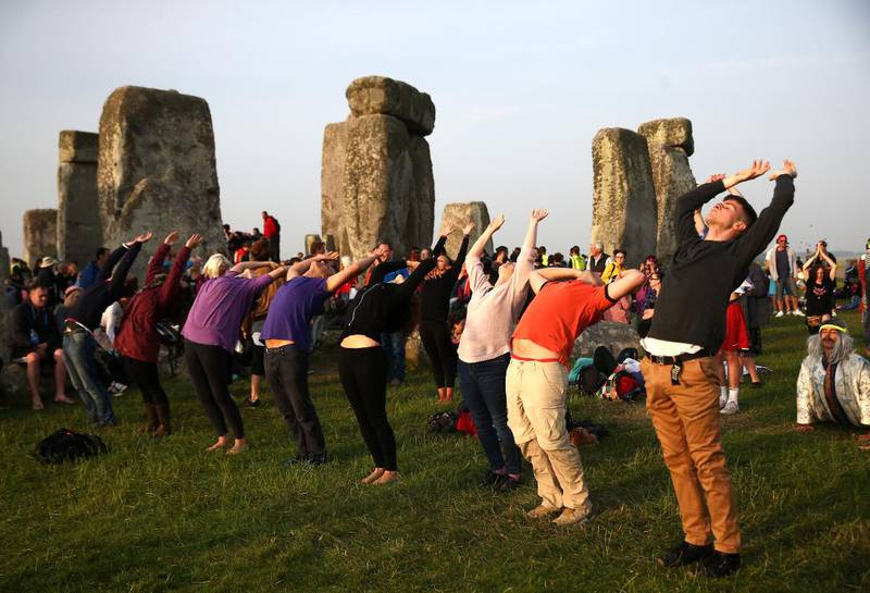 Bildet viser en rekke mennesker. De strekker armene i været og bøyer seg bakover. Bak dem står steinsøylene som utgjør monumentet Stonehenge.