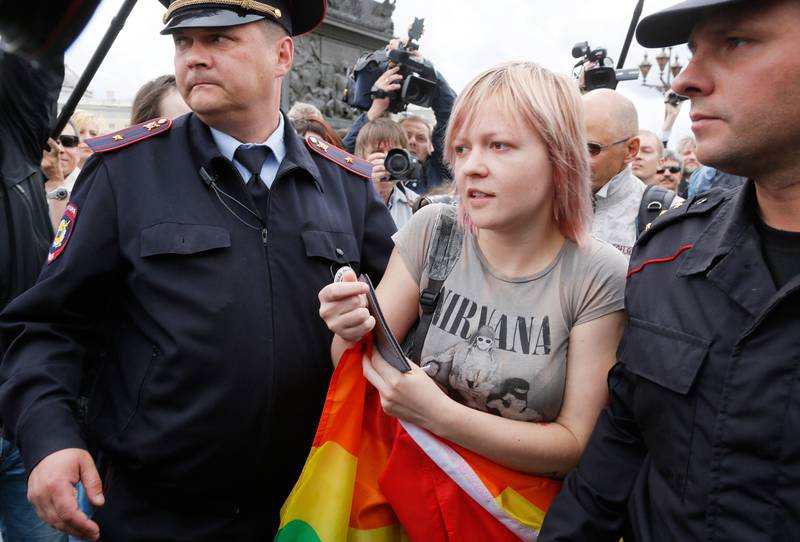 Bildet viser en kvinne med regnbueflagg som føres bort at politiet.