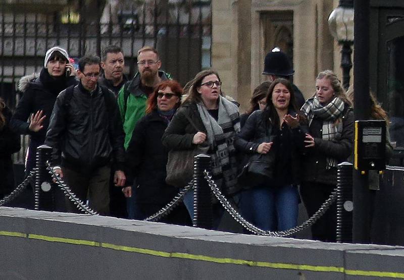 Bildet viser folk som må dra fra området rundt parlamentet onsdag. En kvinne snakker i telefon og noen ser redde ut. 