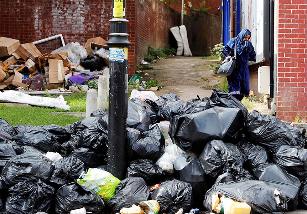 Bildet viser en dame som går forbi et berg av sorte søppelsekker. Hun holder seg for nesen.