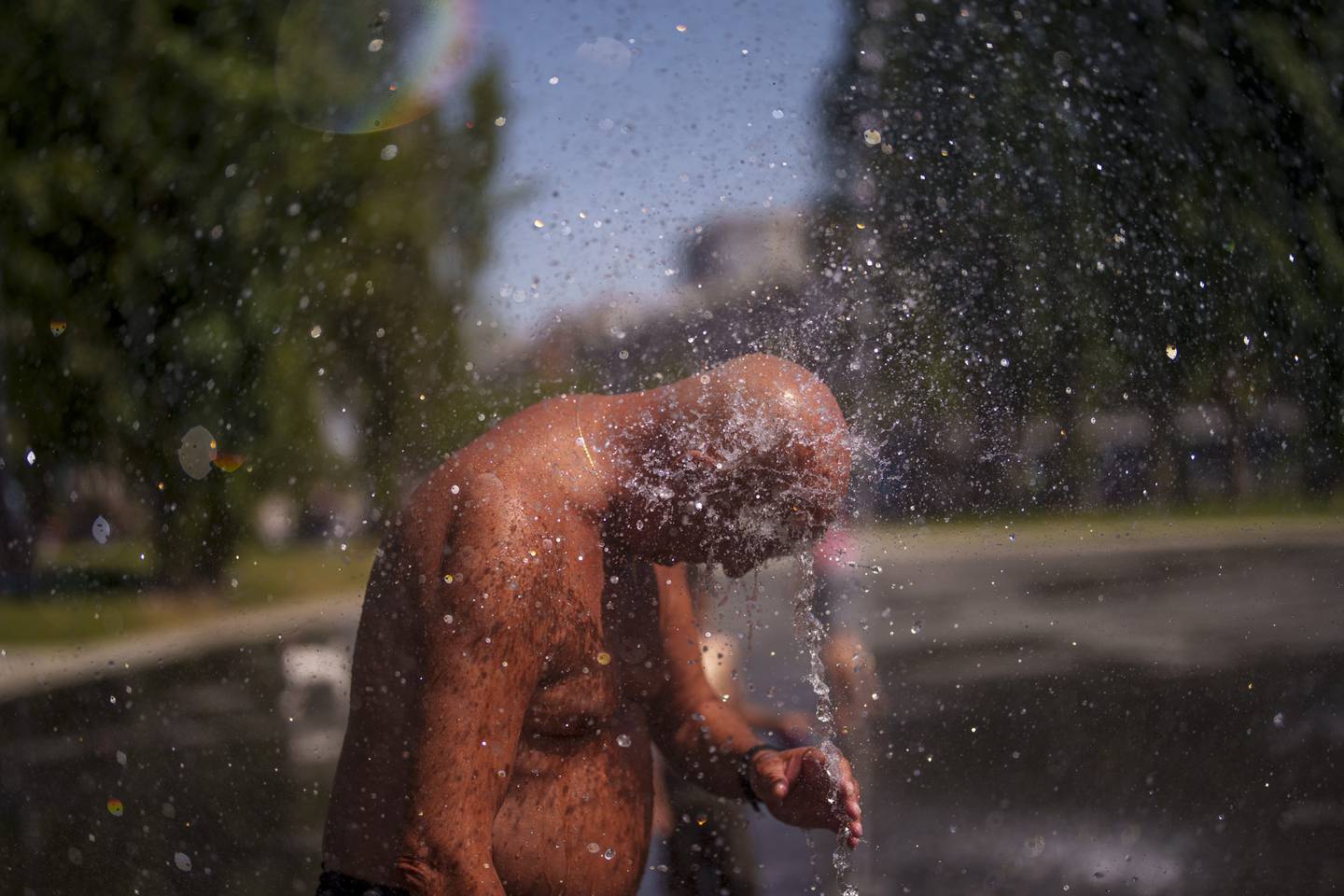 Bildet viser en mann i Madrid som kjøler seg ned med vann.
