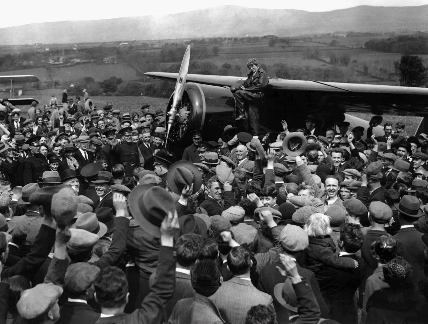 Bildet er av en stor folkemengde. De står rundt et fly. Amelia Earhart sitter og lener seg mot flyet. Arkivfoto: AP / NTB