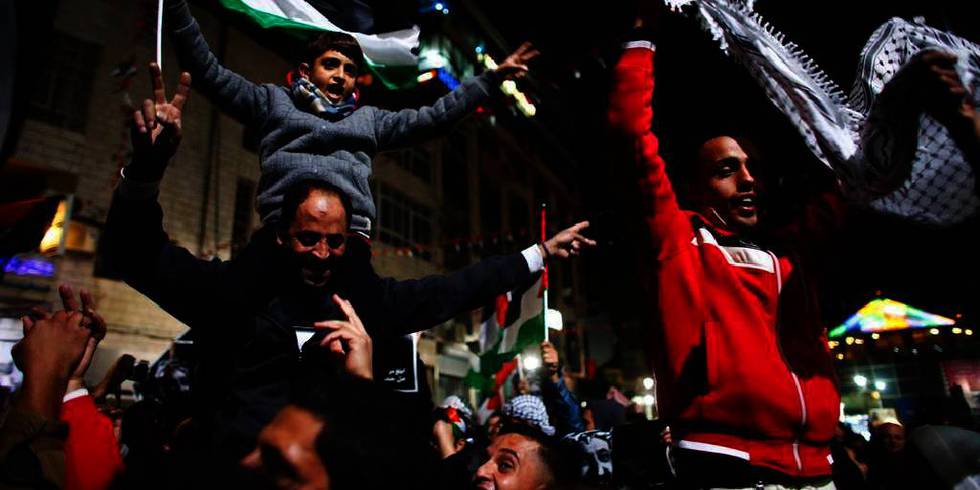 Bildet viser mennesker som feirer i gatene i Rammallah på Vestbredden. EN liten gutt sitter på skuldrene til en mann. Gutten holder et palestinsk flagg. 