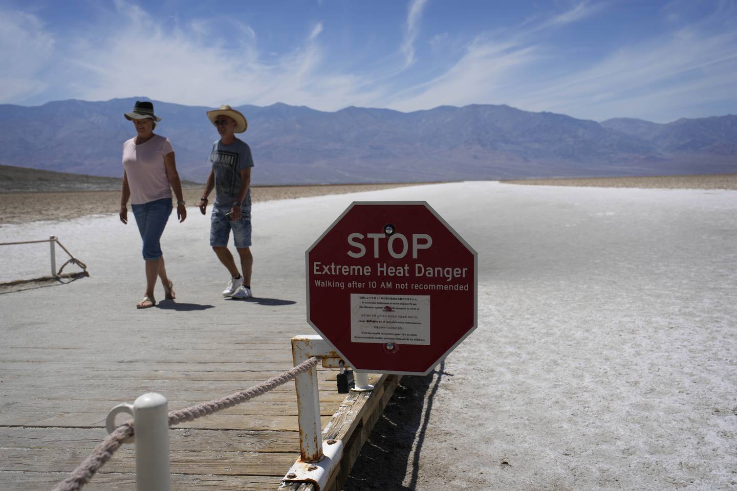 To personer ute i ørkenen med solhatter på. Foran dem er et stopskilt hvor det står "extreme heat danger".