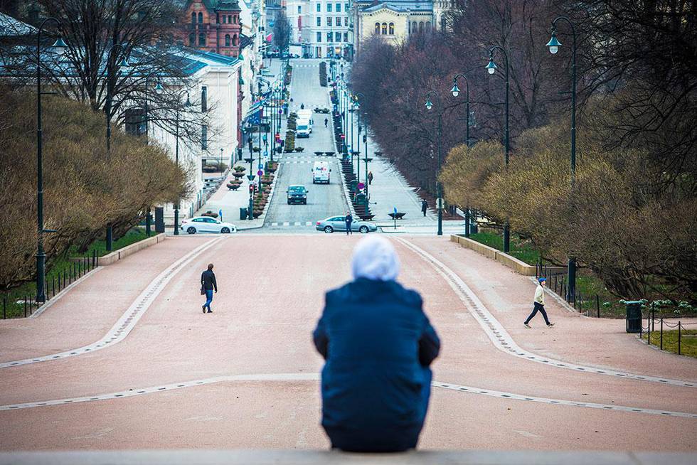 Bildet viser en person som sitter på toppen av Karl Johans gate i Oslo. Det er lite folk i byen. Mange jobber fra hjemmene sine som følge av korona-viruset. Det gjør at det er færre som reiser inn til Oslo og andre store byer. 