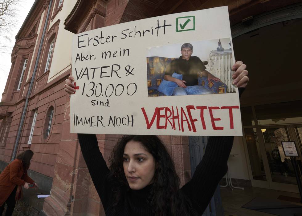 Bildet viser en kvinne med en plakat som demonstrerte utenfor rettslokalet i Koblenz i februar i fjor, da rettssaken mot Anwar Raslan startet. Foto: AP / NTB