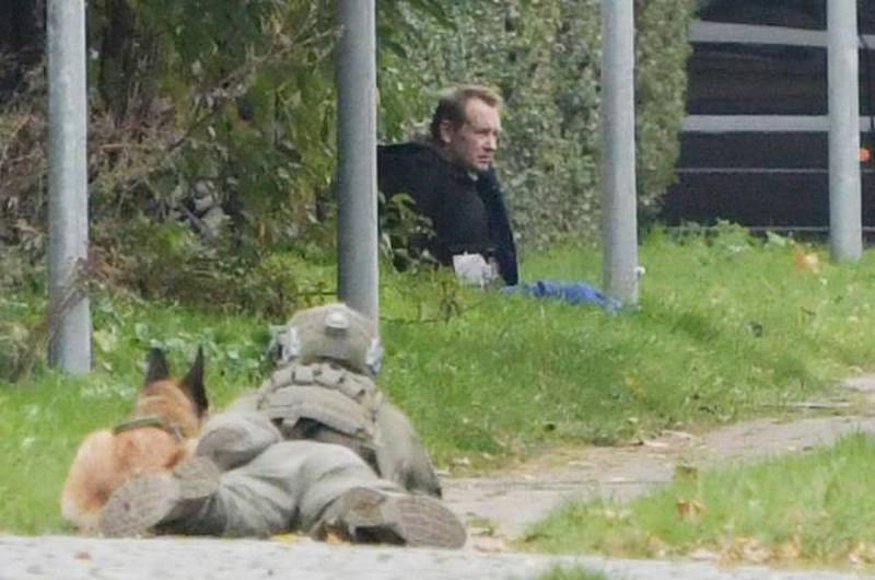 Bildet er av en politimann som ligger på bakken med et våpen. Det peker mot en mann som sitter ved en busk. Det er drapsdømte Peter Madsen. Han har noe festet på magen. Han påsto at det var en bombe. En politihund sitter også klar ved siden av politimannen.