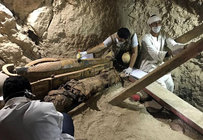 Bildet viser arkeologer som undersøker en trekiste. Ved siden av kisten ligger en mumie.