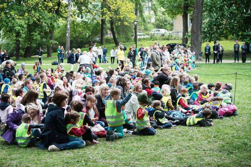 Bildet viser mange barn fra barnehager som sitter i gresset i skulpturparken.