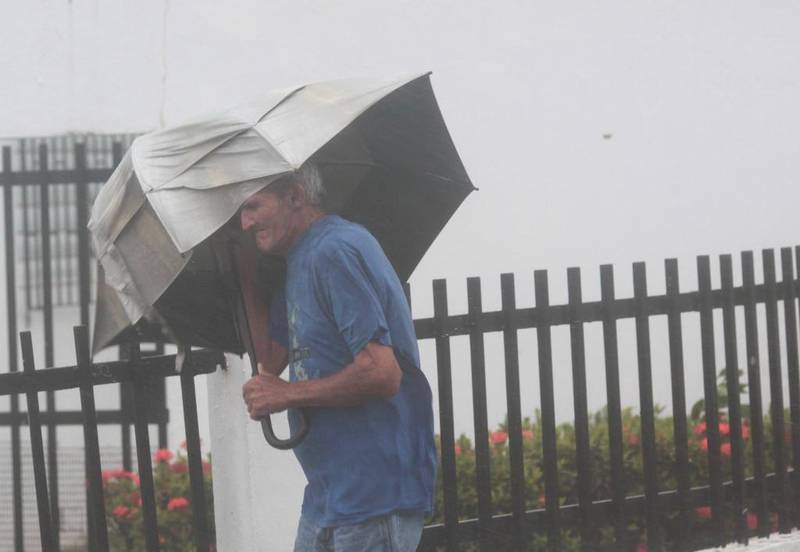 Bildet viser en mann som går i vinden med paraply.