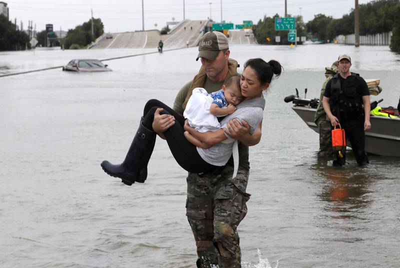 Bildet viser en mann som bærer en kvinne og barnet hennes ut av vannet.