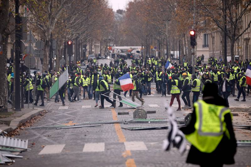 Bildet viser folk som løper i gatene i Frankrike. De har gule vester og masker på.