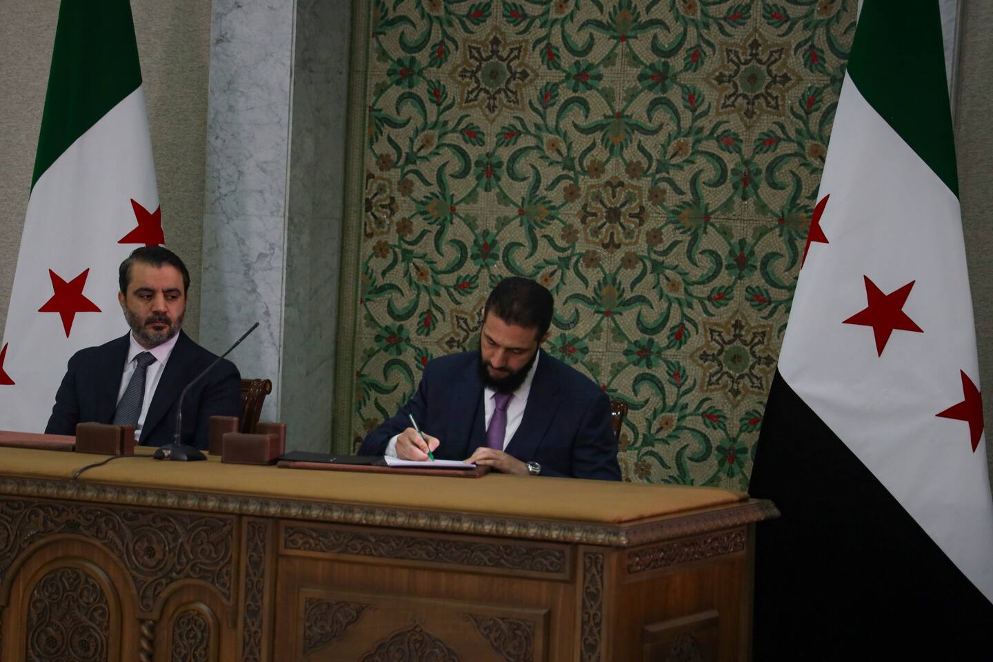 Bildet viser Ahmed al-Sharaa som signerer grunnlovserklæringeni Syria. Foto: AP Photo / Omar Albam / NTB