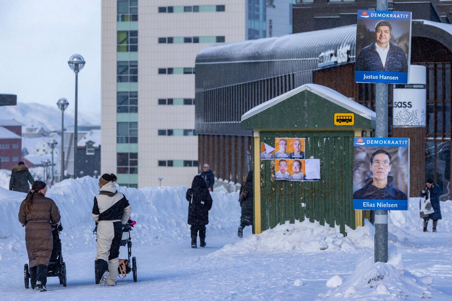 Bildet viser folk som går forbi plakater av grønlandske politikere. Foto: Odd ANDERSEN / AFP / NTB