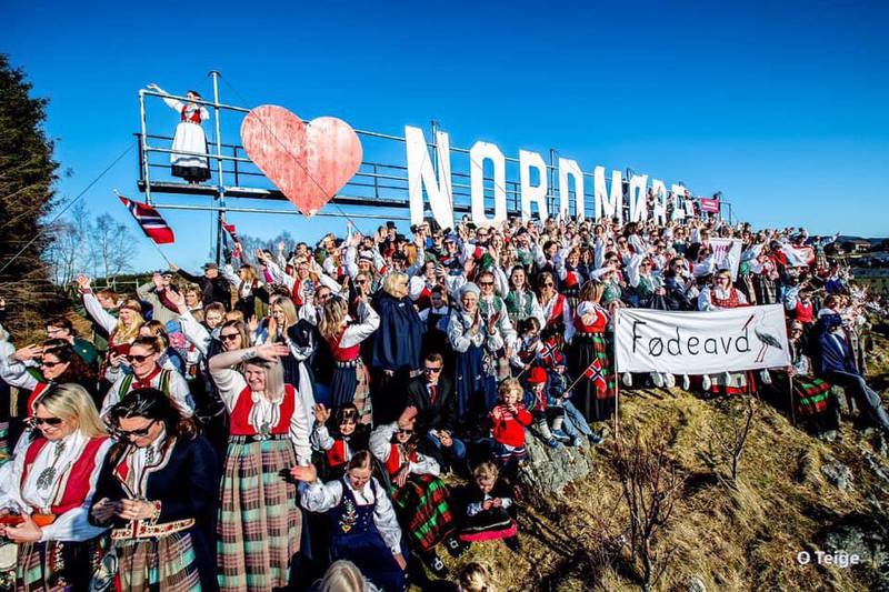 Bildet viser mange kvinner i bunad. De står foran et stort skilt med hjerte og teksten «Nordmøre». Bunadsgeriljaen kjemper for å beholde fødeavdelingen i Kristiansund.