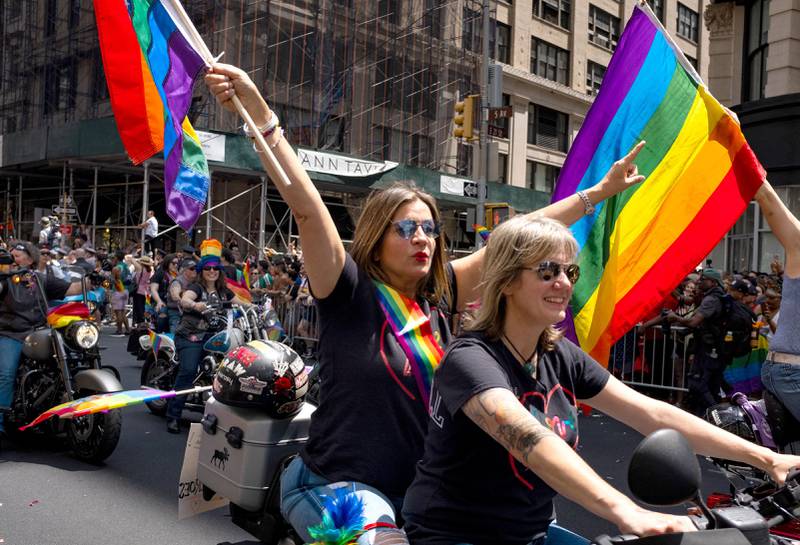 Bildet viser et kvinnelig par på motorsykkel. Den ene har et regnbueflagg.