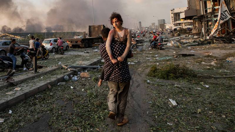Bildet viser en mann som bærer ei ung jente ut av ruinene etter en eksplosjon.