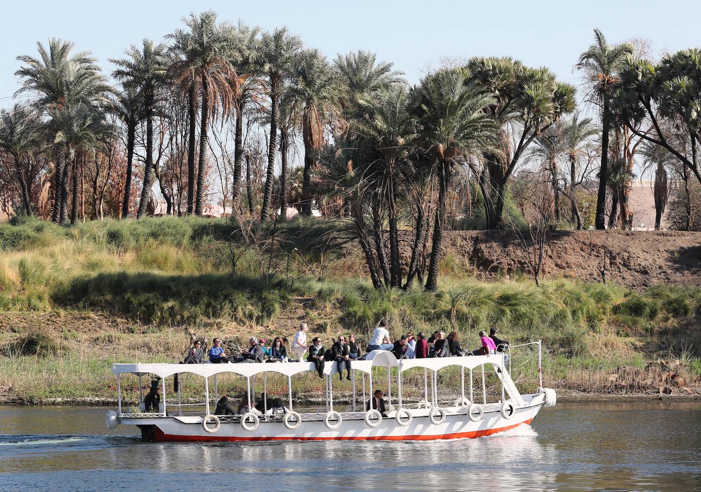 Bildet viser en elvebåt på Nilen. Folk i båten ser utover gresset langs elven. Palmene er grønne og frodige. Dette er i kontrast til ørkensanden som sees i det fjerne.