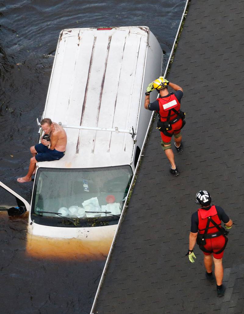 Bildet viser en mann som sitter på taket av den oversvømte bilen sin.
