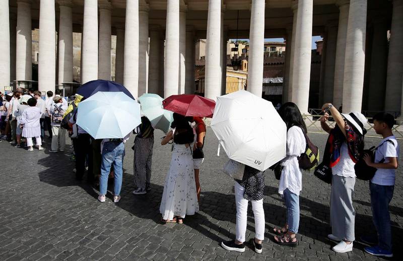 Bildet viser folk med paraplyer i sola på Sankt Peters-plassen i Vatikanstaten.