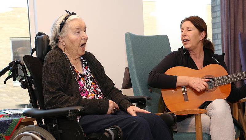 Bildet viser 91 år gamle Kjellaug som følger med på julesangen. Aktivitetskonsulent Mona Tørrissen sitter ved siden av henne og spiller gitar og synger. 