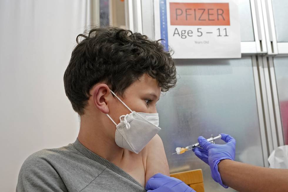 Bildet er av en ung gutt med munnbind som får en sprøyte med koronavaksine i armen. Foto: Ted S. Warren / AP / NTB