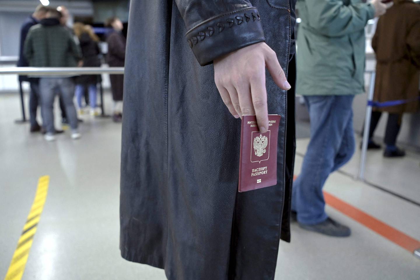 En person med en svart frakk holder et russisk pass i hånden.