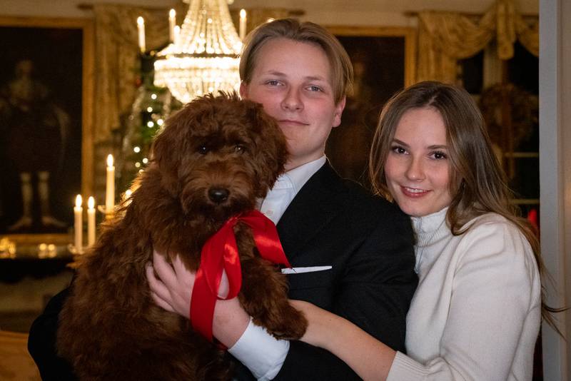 Bildet er av Prins Sverre Magnus og Prinsesse Ingrid Alexandra som løfter opp hunden Molly Fiskebolle. Den er en brun labradoodle og den har rød sløyfe. Foto: Simen Sund, Det kongelige hoff / NTB
