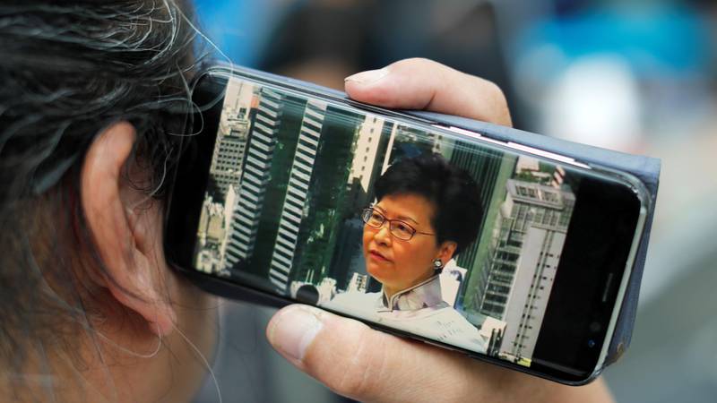 Bildet viser en person som lytter til en tale med Carrie Lam via mobiltelefonen sin.